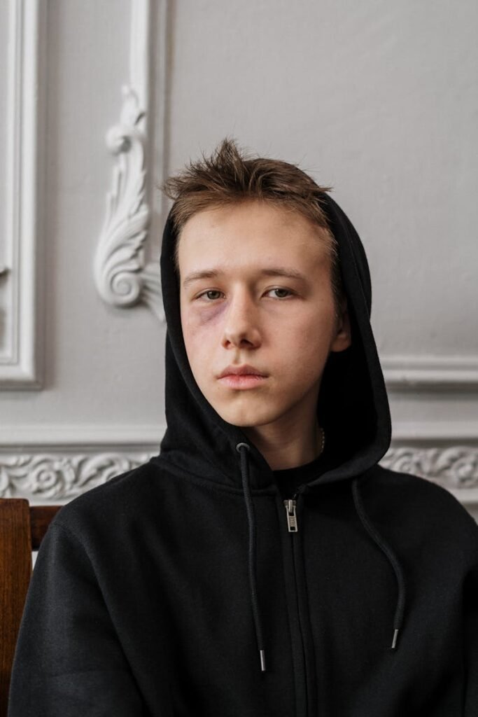 Moody portrait of a teenage boy with a black hoodie and subtle bruise, indoors.